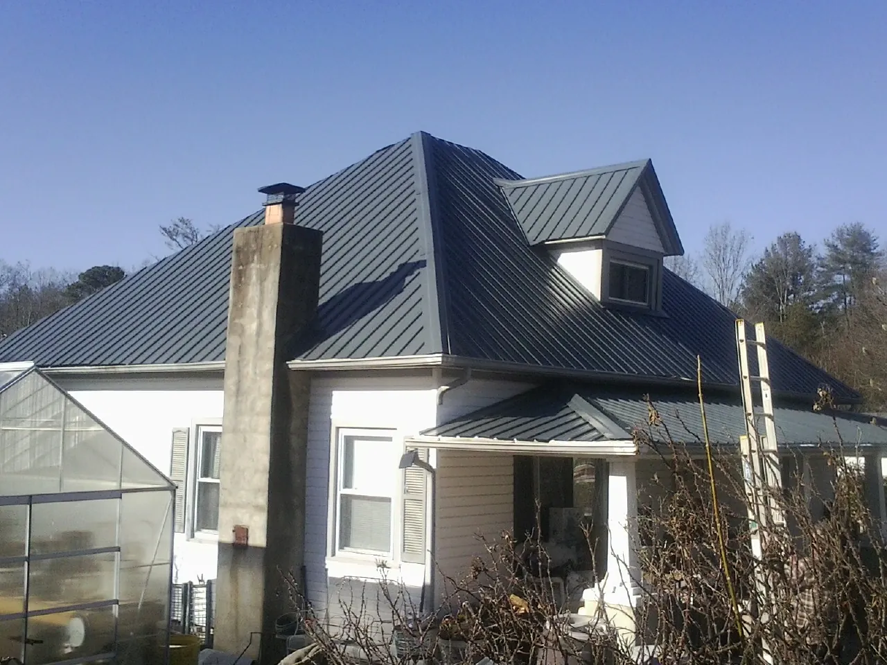 Dark blue standing seam metal roof on a white farmhouse with dormer — Slate & Tile Roof Repair by Roofing Brothers in Milburn