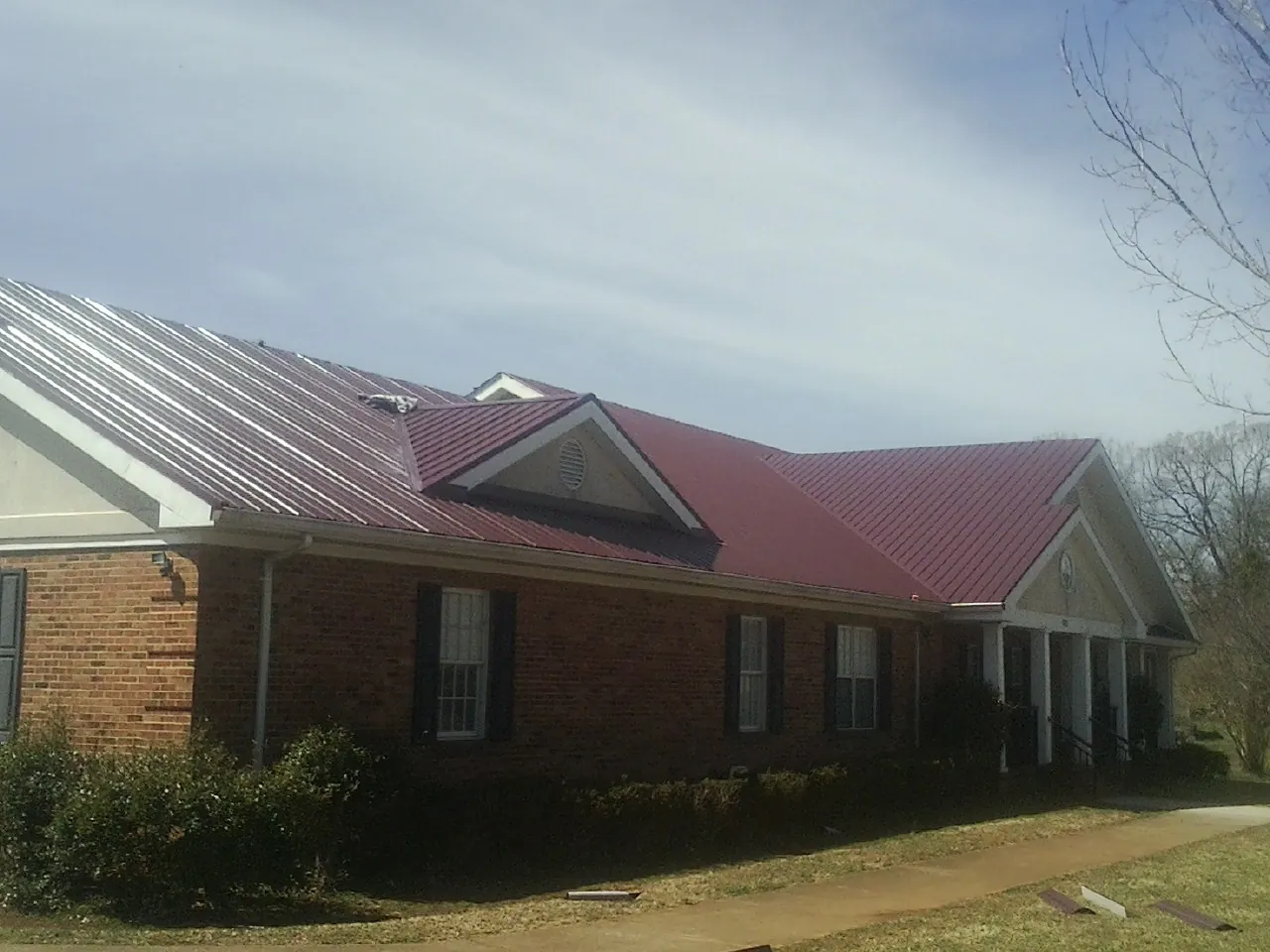 Red metal roof with gabled entries on a long brick building, from a Hail Damage Roof Repair job in Milburn