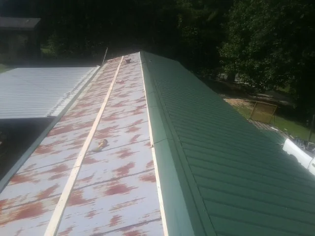 Old rusted panels beside newly installed green metal roofing — Wind Damage Roof Repair by Roofing Brothers in Milburn