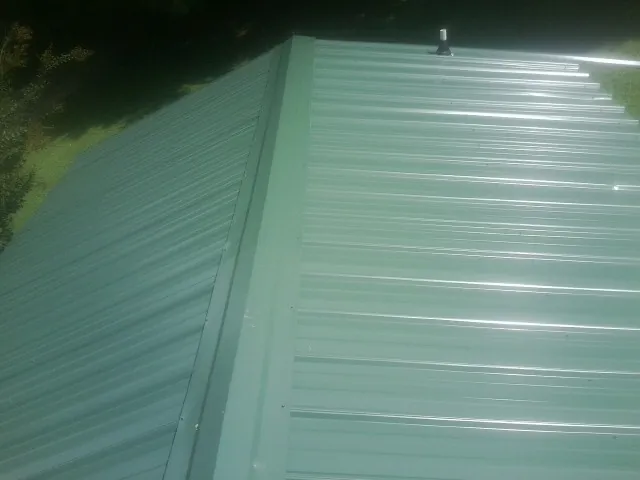 New green metal panels meeting at the ridge of a roof — Flat Roof Repair work by our crew in Milburn