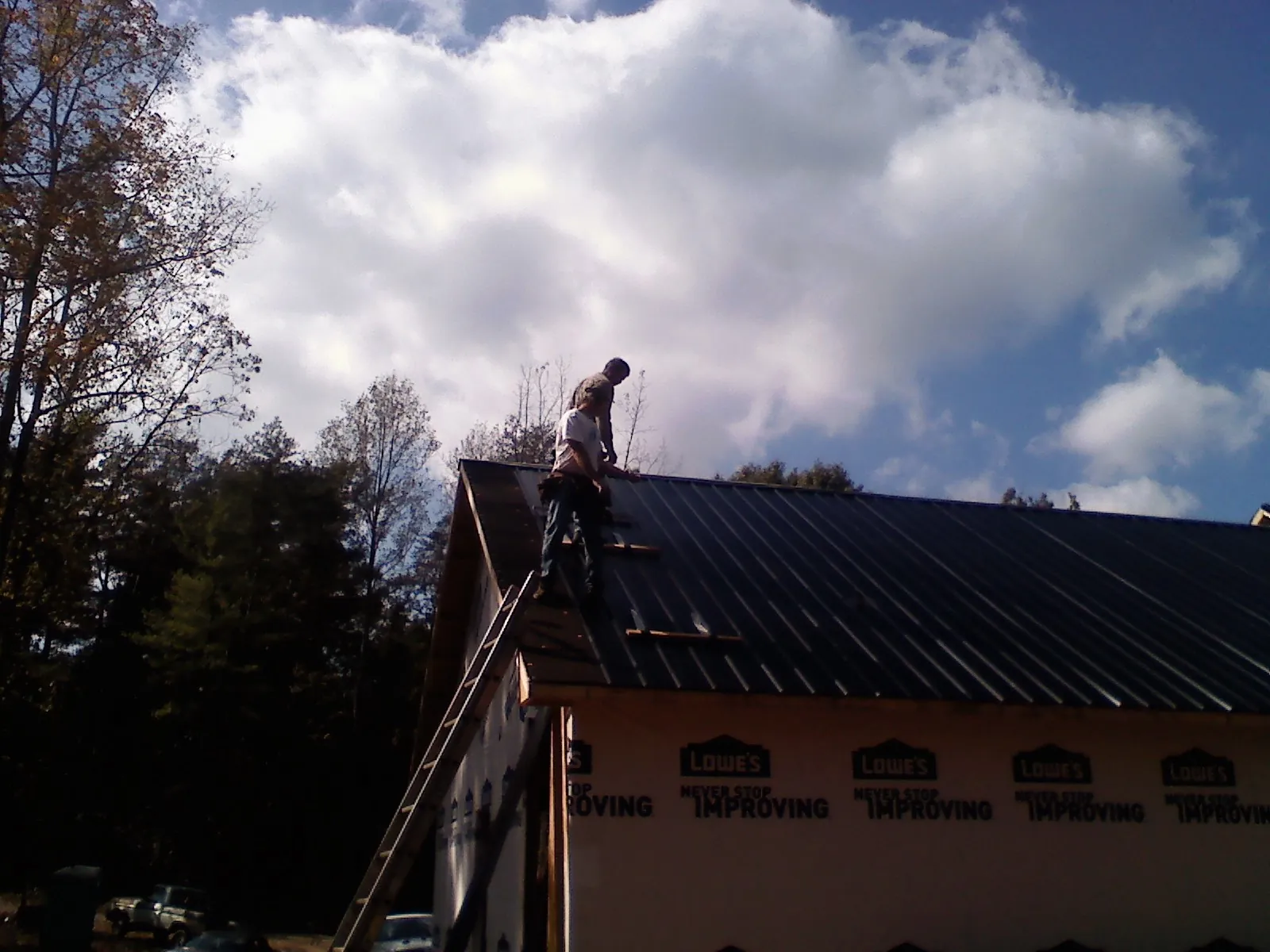 Roofer fastening dark metal panels high against a cloudy sky, from a Roof Inspection job in Milburn