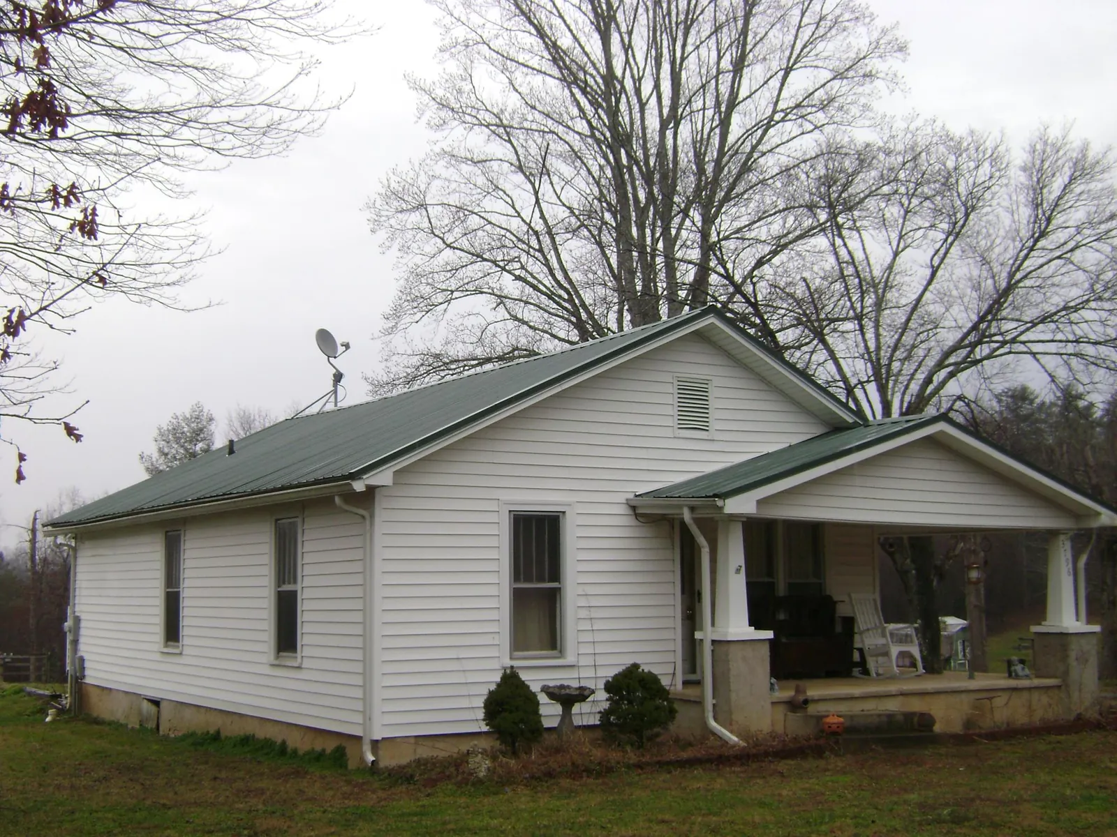 Green metal roof on a white bungalow with a side porch in Milburn