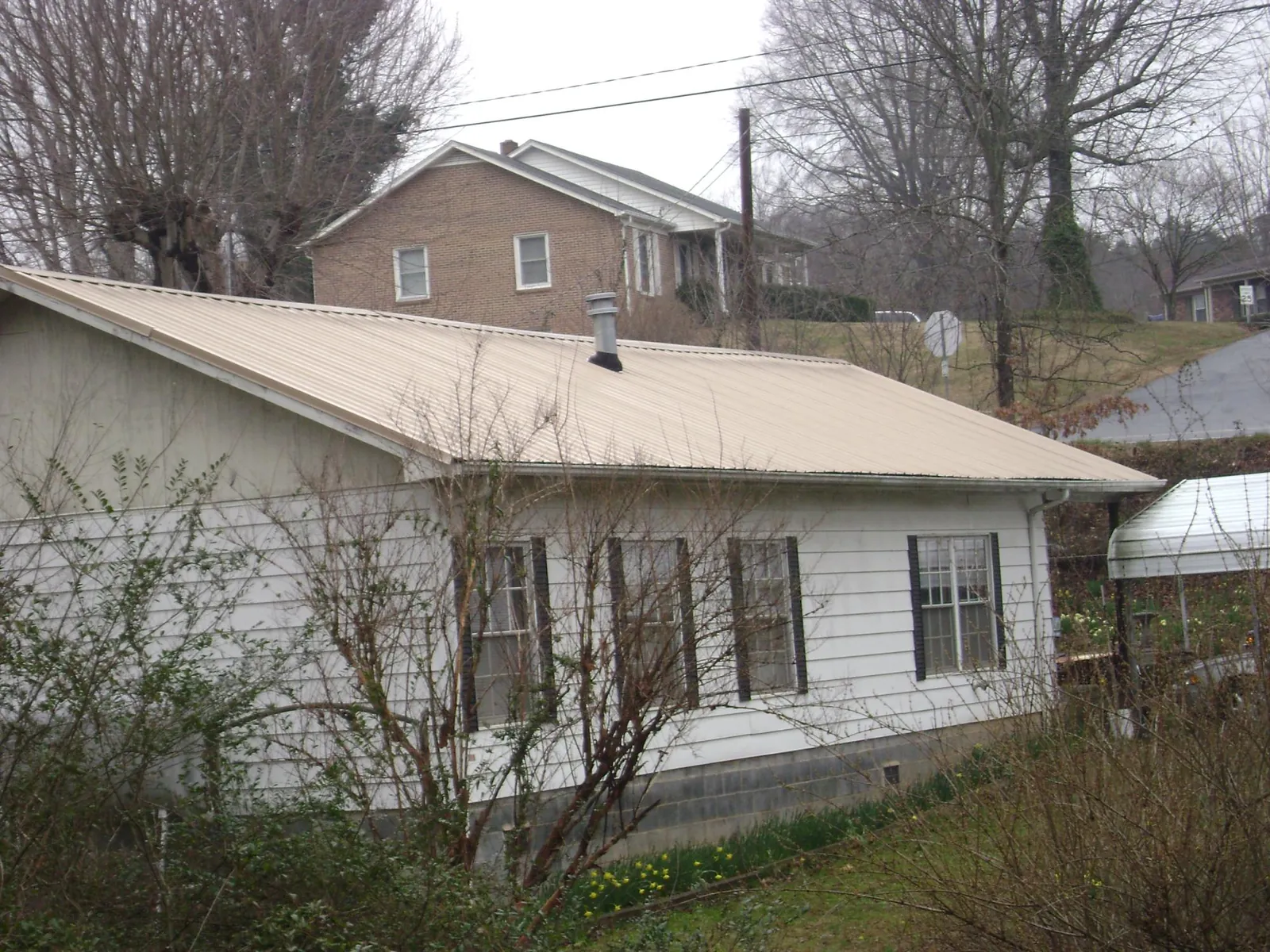 Tan metal roof on a white sided house set into a hillside — Commercial Roofing by Roofing Brothers in Milburn