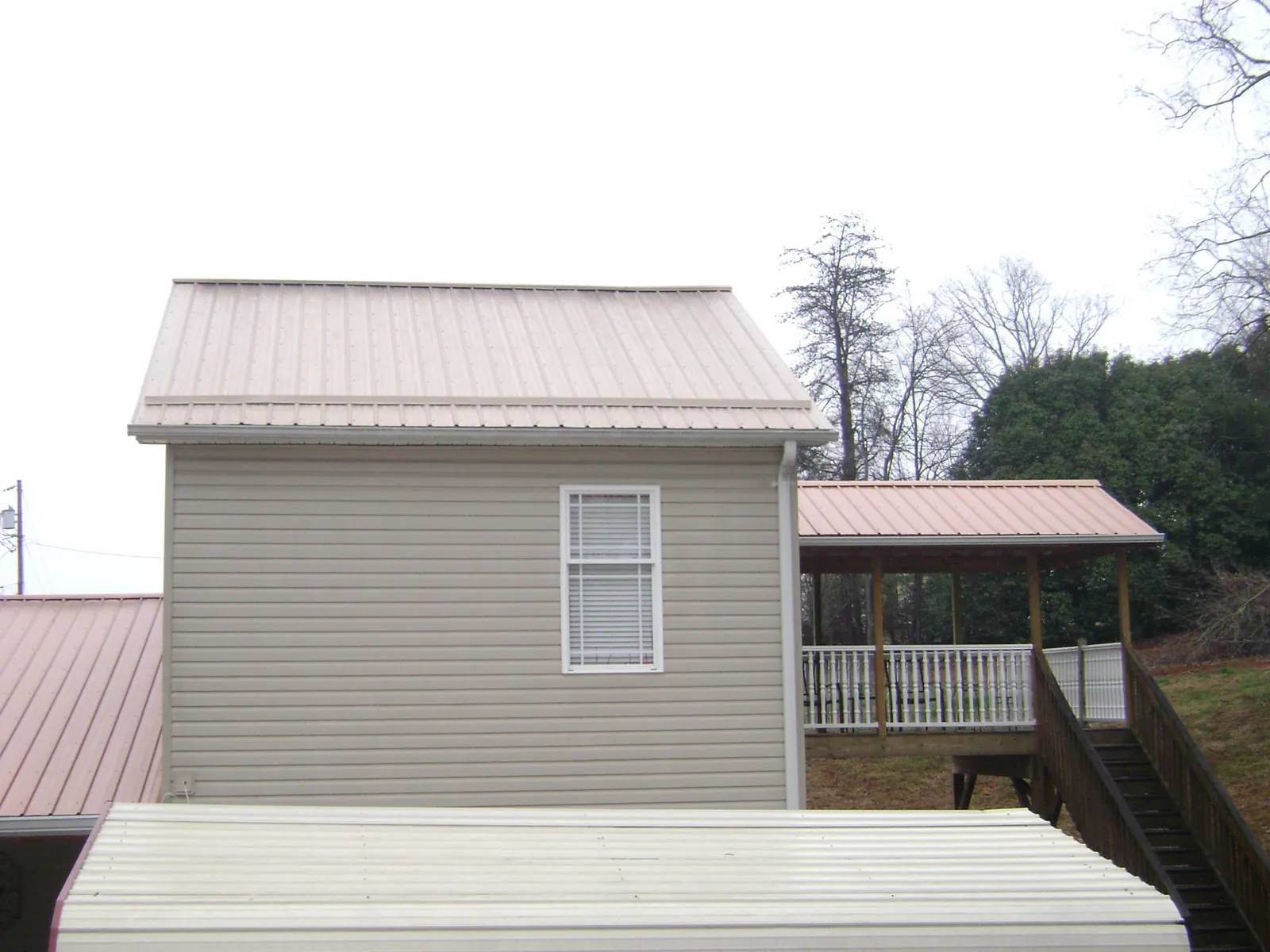 Tan metal roofs on a two story addition and attached porch, from a Roof Replacement job in Milburn